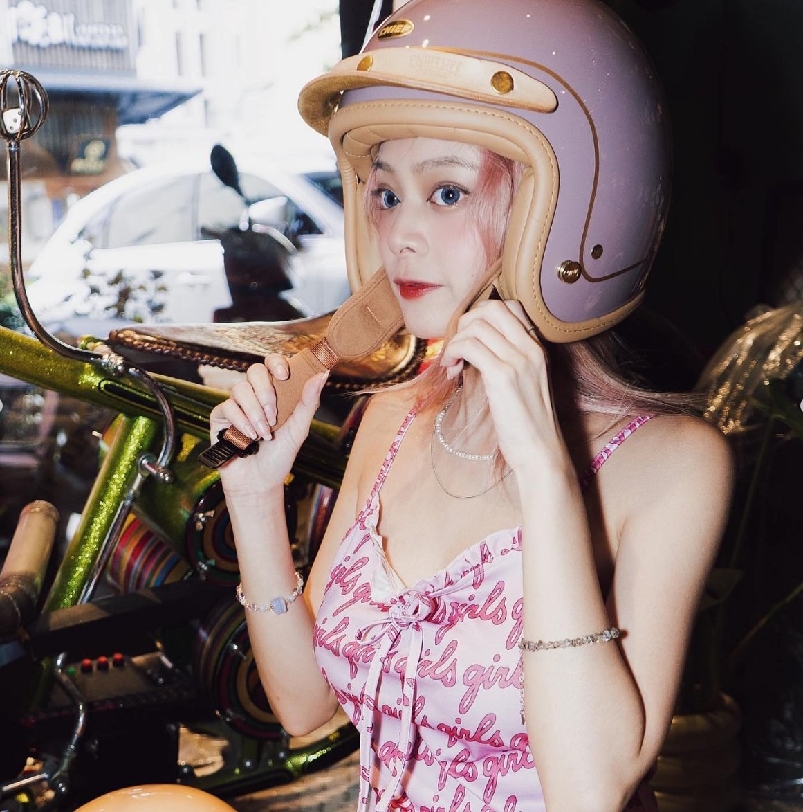 Campaign: model fastening the chin strap of a lilac open-face helmet, candid shot without brand overlay
